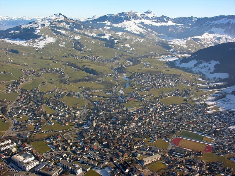 Luftaufnahme von Appenzell mit weitläufigen Hügeln, verstreuten Häusern und schneebedeckten Bergen.