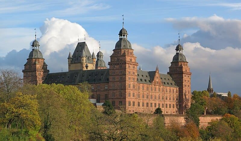 Historisches Sandsteinschloss in Aschaffenburg mit markanten Türmen über farbigem Laub.