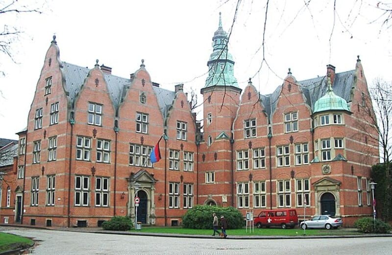 Historisches Backsteingebäude in Aurich mit Türmchen, Giebeln und symmetrischen Fensterreihen.