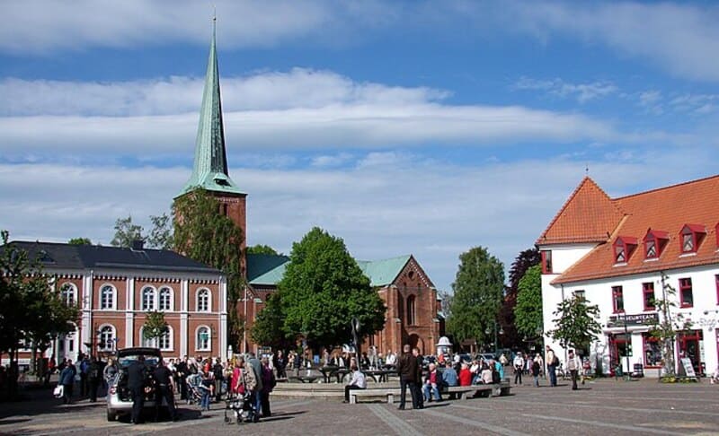 Blick auf den Platz in Bad Segeberg mit rotem Backsteinbau, Kirchturm und Menschen im Sonnenschein.