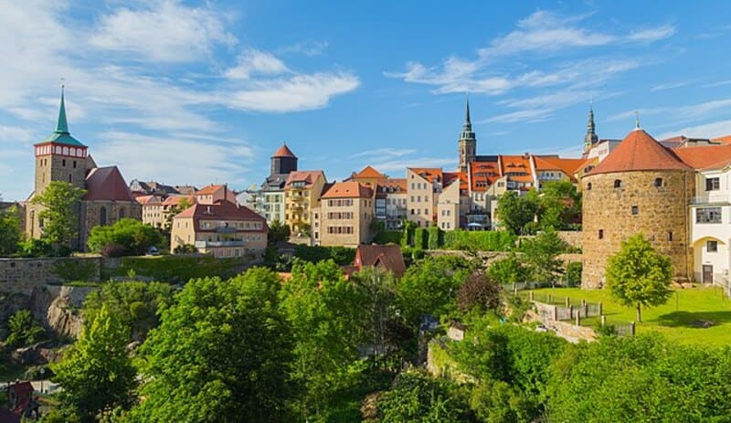 Historische Altstadt von Bautzen mit Türmen, farbigen Dächern und grüner Landschaft im Sonnenlicht.