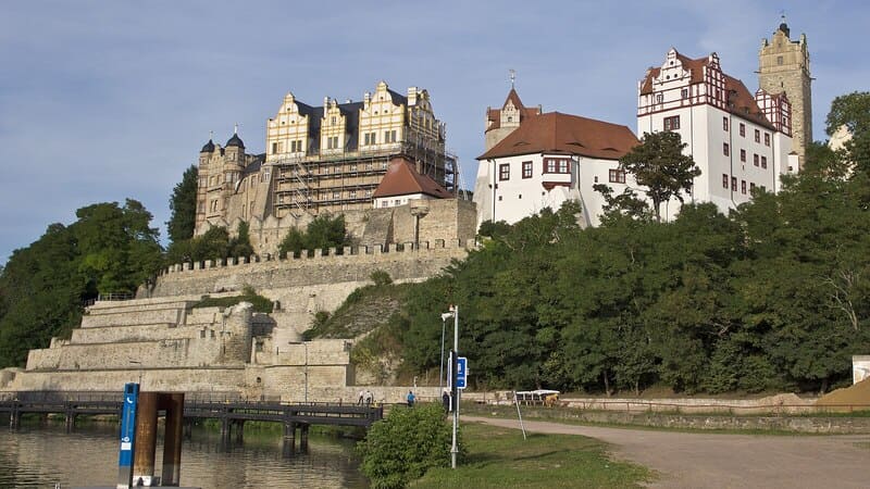 Blick auf das Schloss Bernburg mit terrassierten Mauern, Fachwerkdetails und Uferbereich an der Saale.