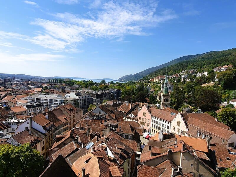 Blick über die Altstadt von Biel mit roten Dächern, Kirche und bewaldetem Hang.