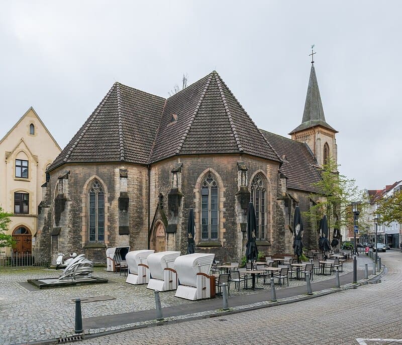 Historische Kirche in Bielefeld mit gotischen Fenstern und Außenbestuhlung auf dem Platz.