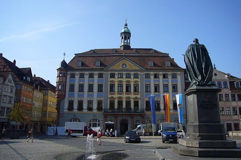 Historisches Rathaus von Coburg mit farbiger Fassade, Brunnen und Statue auf dem Marktplatz.