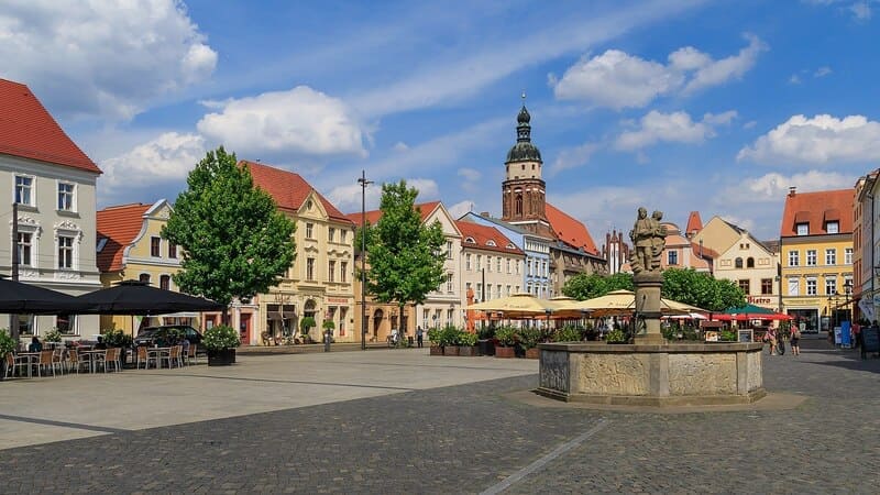 Marktplatz in Cottbus mit Brunnen, Caféterrassen und bunt restaurierten Fassaden bei Sonnenschein.