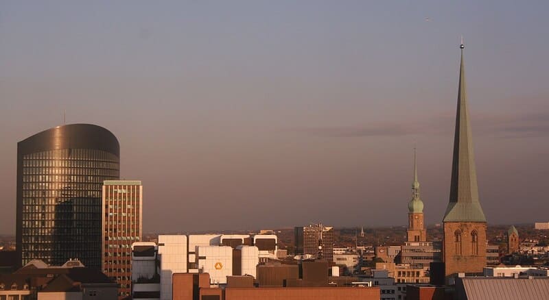 Skyline von Dortmund mit modernem Hochhaus und markanten Kirchtürmen im Abendlicht.