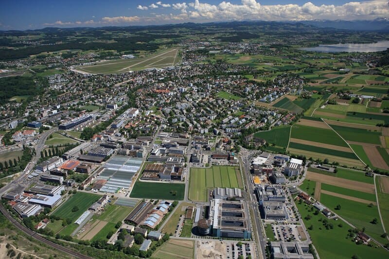 Luftaufnahme von Dübendorf, Schweiz, mit Industriegebieten, Wohnvierteln und umliegenden Feldern.