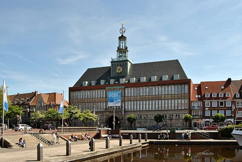 Rathaus in Emden mit Uhrturm, breitem Platz und Wasserbecken im Vordergrund.