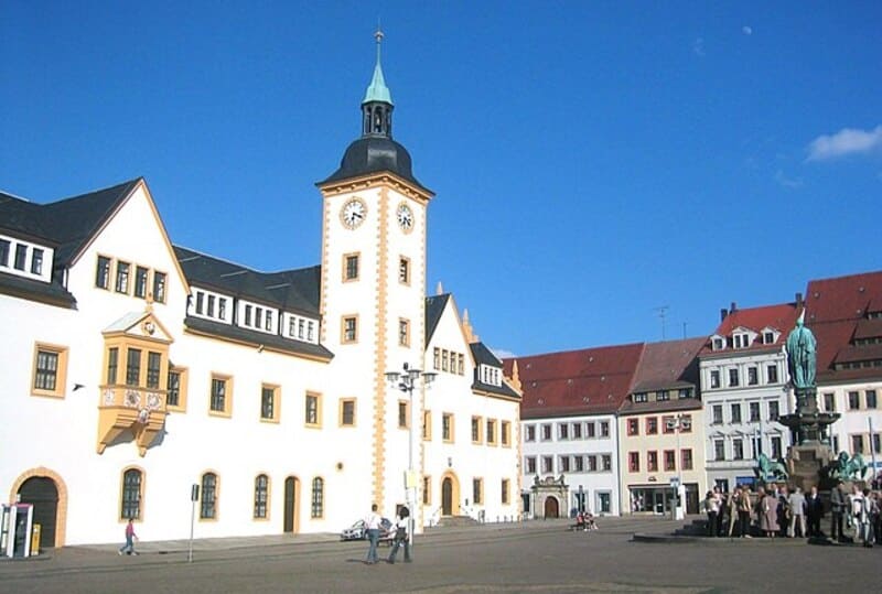 Coreflow-Freiberg-Hero Marktplatz von Freiberg mit hellem Rathaus, Uhrturm und umliegenden historischen Gebäuden.