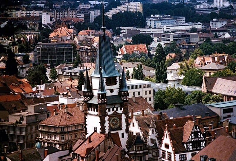 Stadtansicht von Freiburg im Breisgau mit markantem historischen Turm über dicht bebauten Vierteln.