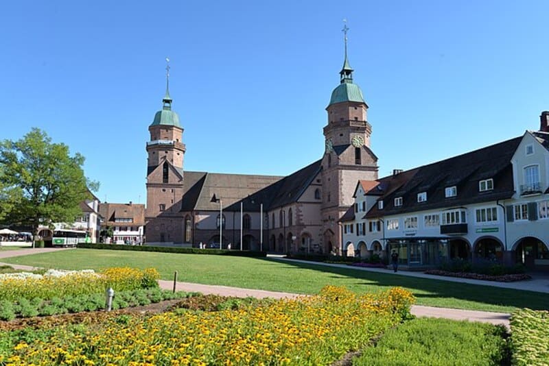 Blumenbeet und Grünfläche vor großer Kirche mit Doppeltürmen im Zentrum von Freudenstadt.