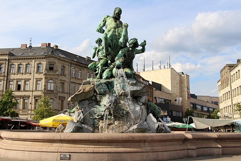 Stein- und Bronze-Brunnen mit mythologischen Figuren vor umliegenden Gebäuden im Stadtzentrum Fürths.