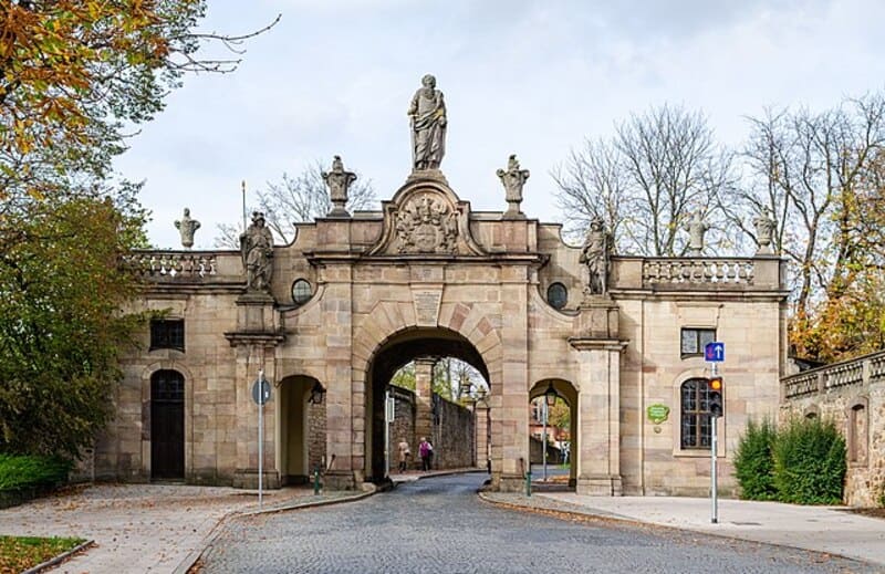 Historisches Tor in Fulda mit Sandsteinbögen, Figuren und herbstlichen Bäumen im Hintergrund.