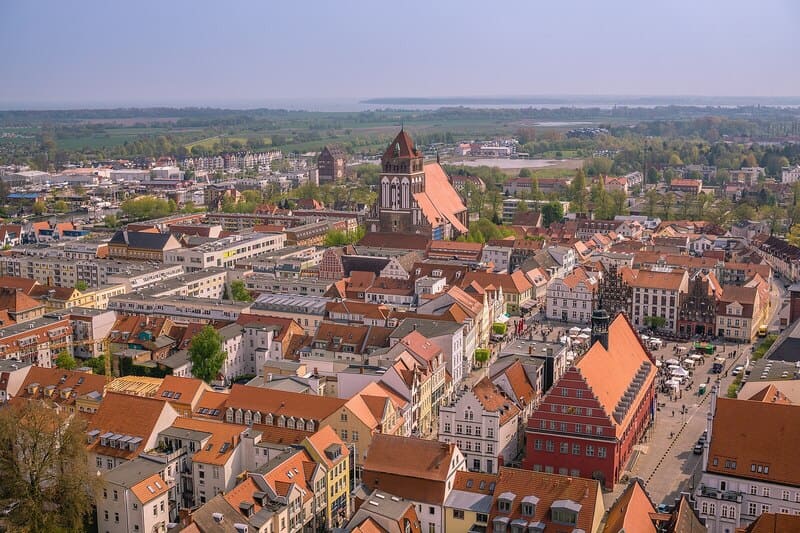 Luftaufnahme von Greifswald mit roter Backsteinkirche, dichtem Altstadtkern und weitem Blick ins Umland
