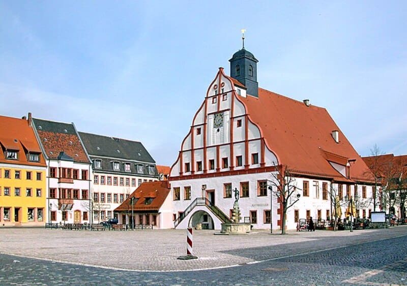 Historisches Rathaus von Grimma mit rotem Dach und umliegenden farbigen Altstadthäusern am Marktplatz.