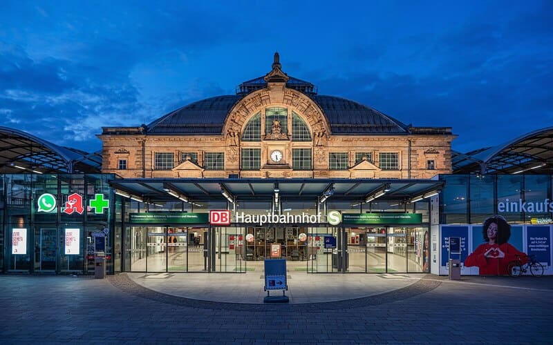 Blick auf den Hauptbahnhof Halle (Saale) mit gläsernem Eingang und erleuchteter Kuppelfront.