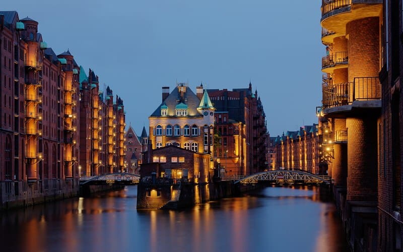 Beleuchtete Backsteingebäude der Hamburger Speicherstadt an einem ruhigen Wasserkanal bei Abendlicht.