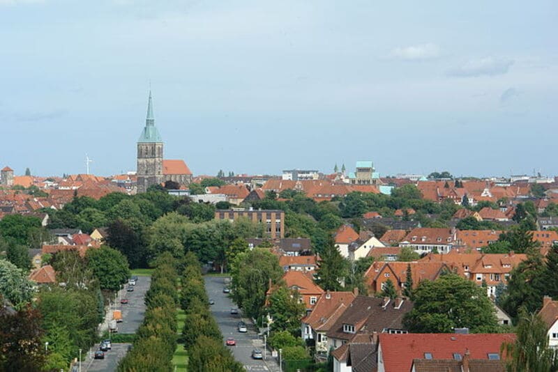 Blick über Hildesheim mit roter Dachlandschaft, breiter Allee und markantem Kirchturm im Hintergrund.