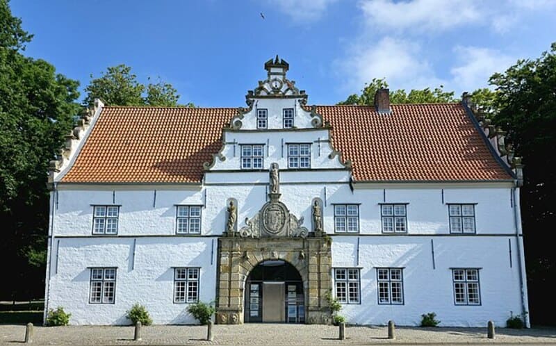Historisches weißes Gebäude in Husum mit verziertem Giebel und großem Rundbogenportal.