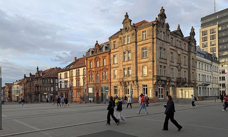 Stadtplatz mit historischen Fassaden, modernen Gebäuden und gehenden Passanten bei Tageslicht in Kaiserslautern.