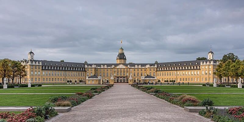 Symmetrischer Blick auf das Karlsruher Schloss mit breitem Weg und gepflegten Gartenanlagen.