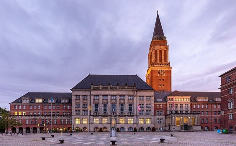 Rathaus Kiel mit beleuchtetem Turm und weitläufigem Platz unter wolkigem Abendhimmel.