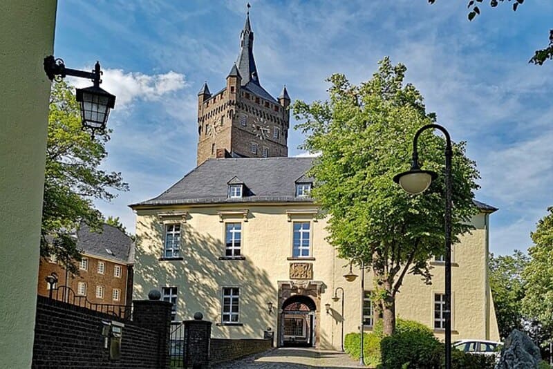Helles zweistöckiges Gebäude mit hohem Backsteinturm und umgebenden Bäumen in Kleve.