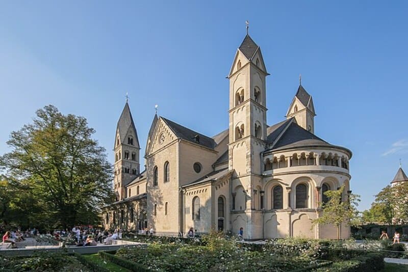 Romanische Kirche mit Türmen und Rundapsis in gepflegter Parkanlage bei Sonnenschein in Koblenz.