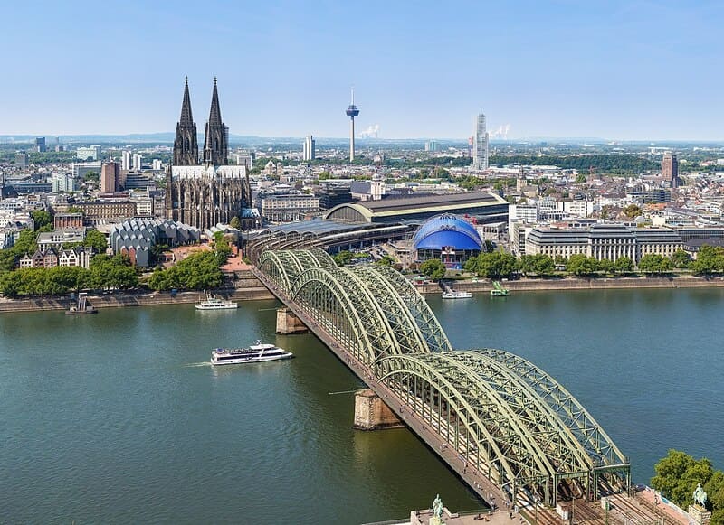 Blick auf den Kölner Dom, die Hohenzollernbrücke und vorbeifahrende Schiffe auf dem Rhein.