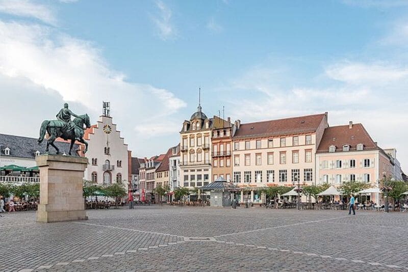 Großer Marktplatz mit Reiterstatue, historischen Fassaden und Cafébestuhlung bei Tageslicht in Landau.