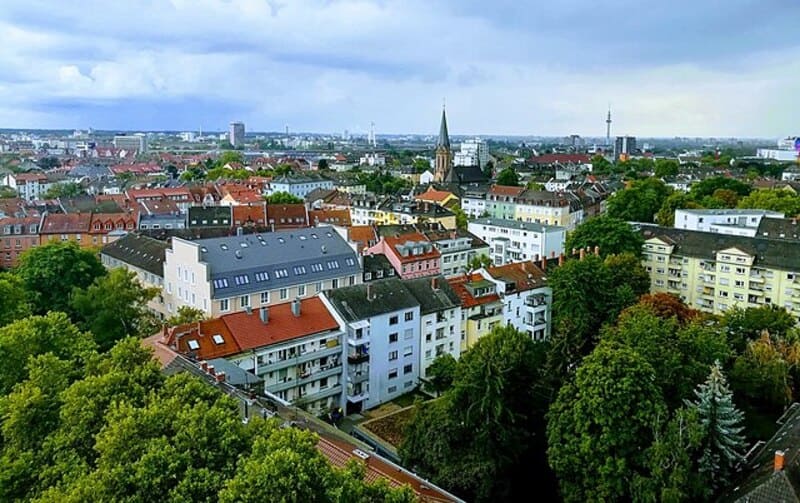 Blick von oben auf dicht bebautes Wohnviertel mit Bäumen und Stadtsilhouette in Ludwigshafen.