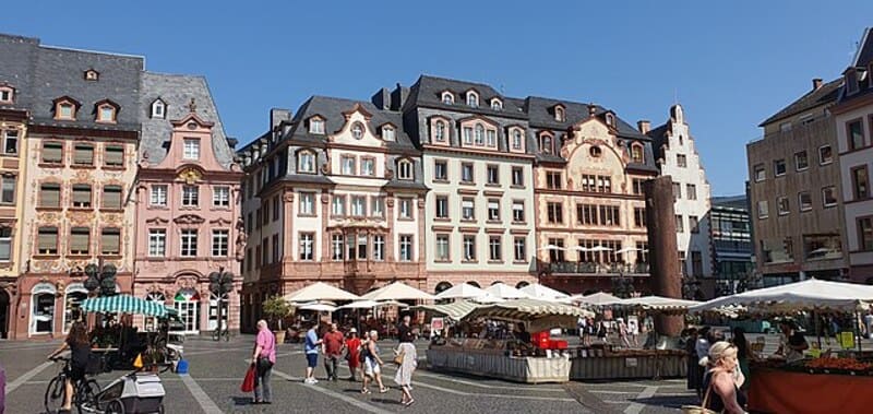 Belebter Marktplatz mit historischen Fassaden, Marktständen und Fußgängern bei Sonnenschein in Mainz.