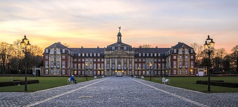 Barockes Schloss mit breit angelegtem Vorplatz und Laternen bei Sonnenuntergang in Münster.
