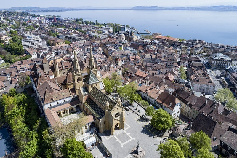 Luftaufnahme der Altstadt von Neuenburg mit markanter Kirche und Blick über den See.