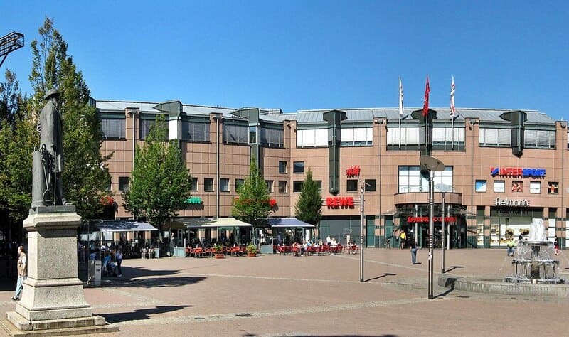 Stadtplatz in Neunkirchen mit Einkaufszentrum, Außengastronomie, Brunnen und klarer Sommerbeleuchtung
