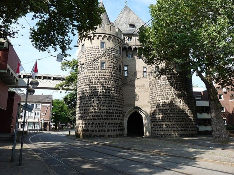Historisches Stadttor mit zwei Rundtürmen an einer Straßenbahnstrecke im Zentrum von Neuss.