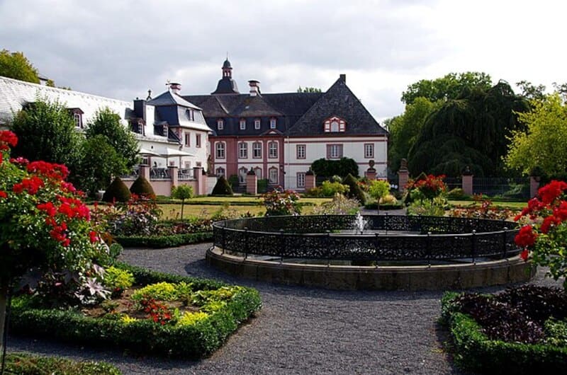 Symmetrische Gartenanlage mit Wasserbecken, Blüten und Schlossfassade im Hintergrund in Neuwied.