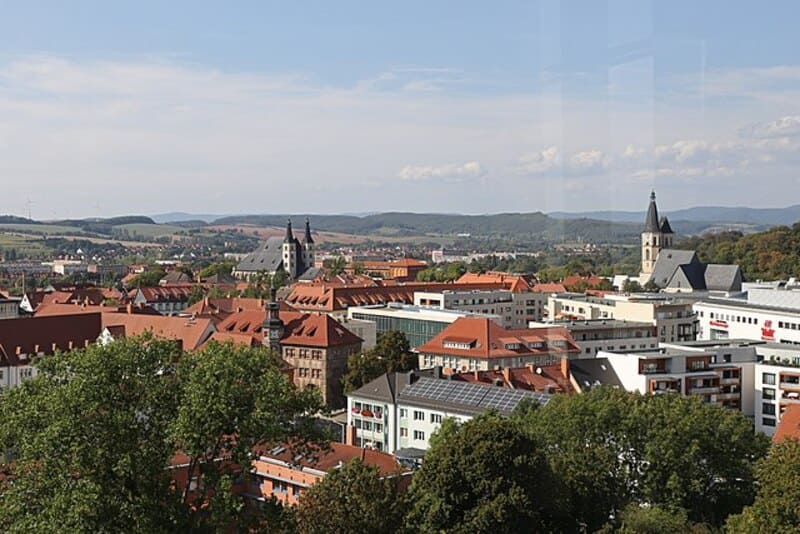 Blick über Nordhausen mit roten Dächern, Stadtzentrum und umgebenden Hügeln im Sonnenlicht.