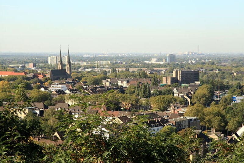 Weitläufige Stadtansicht mit Kirchtürmen, Wohngebieten und viel Grün unter klarem Himmel in Oberhausen.
