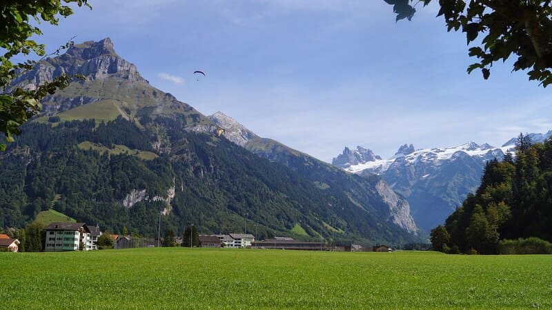 Weite Talansicht in Obwalden mit Dorf, bewaldeten Hängen und schneebedeckten Gipfeln.