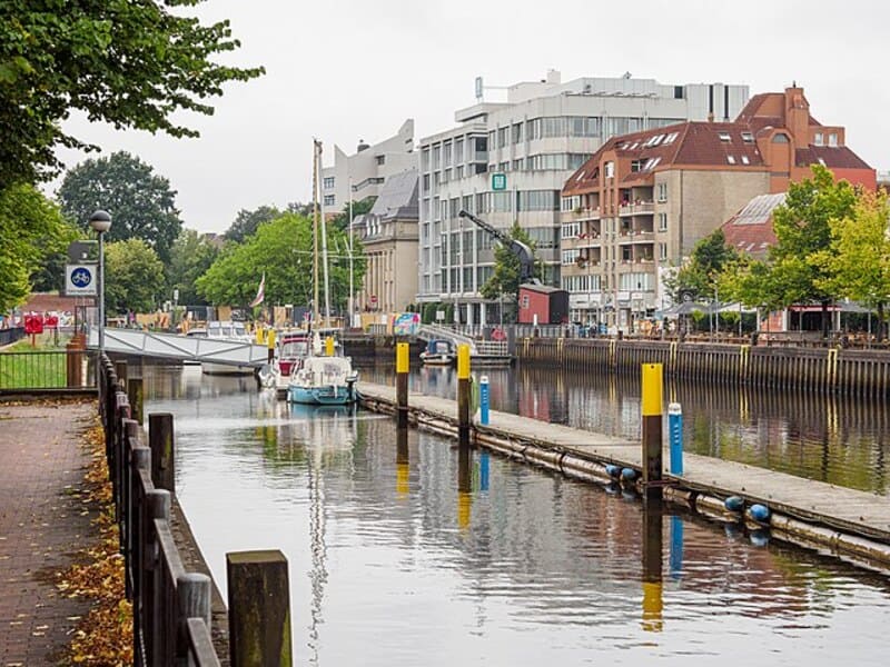 Kanalansicht in Oldenburg mit kleinen Booten, moderner Bebauung und herbstlichen Bäumen am Ufer.