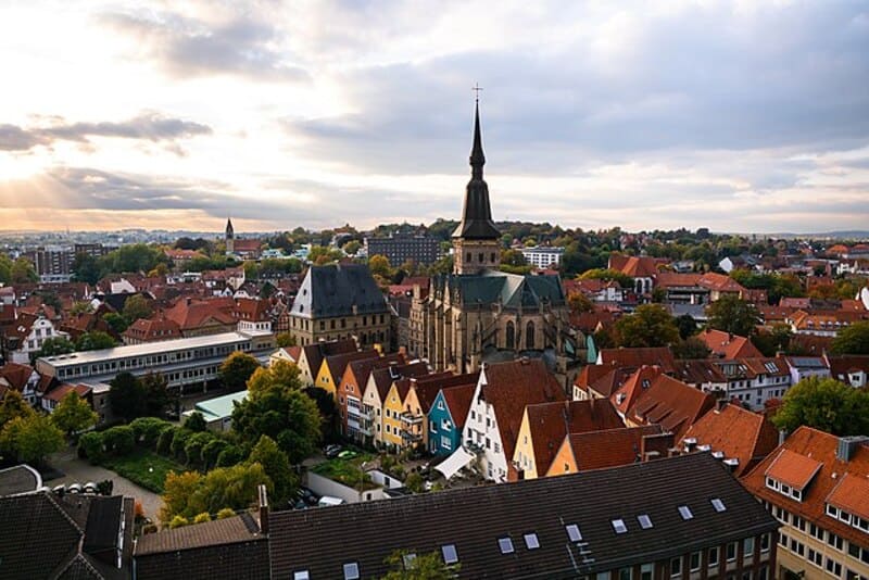 Blick über Osnabrücks Altstadt mit roten Dächern, markanter Kirchturmspitze und dichter Bebauung.