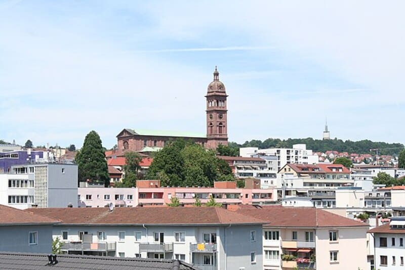 Stadtansicht von Pforzheim mit Wohngebäuden im Vordergrund und markantem Kirchturm auf Anhöhe.