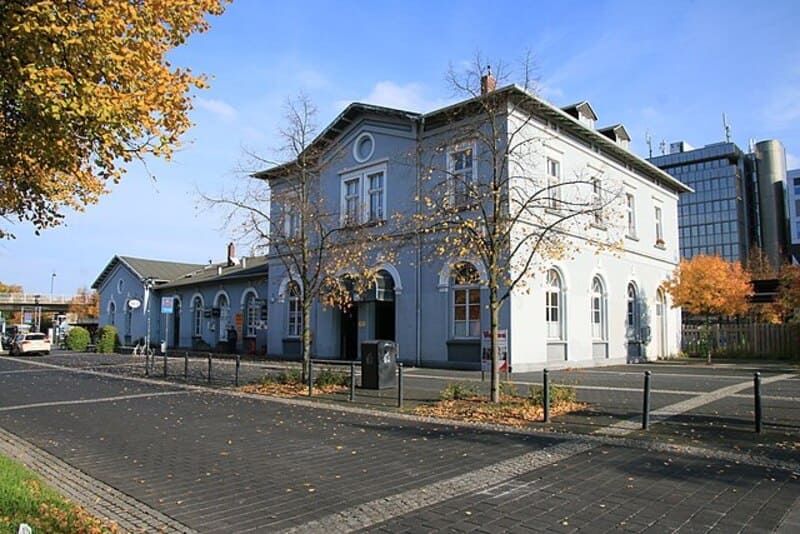Historisches zweistöckiges Bahnhofsgebäude mit hellgrauer Fassade und herbstlichen Bäumen in Ratingen.