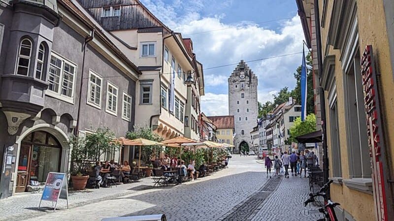 Kopfsteinpflastergasse in Ravensburg mit Cafés und Blick auf den hohen historischen Stadtturm.