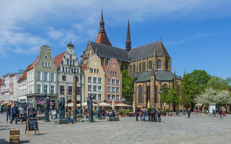Belebter Marktplatz in Rostock mit bunten Giebelhäusern und großer Backsteinkirche im Hintergrund.