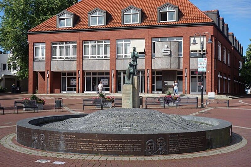 Statue auf Sockel vor öffentlichem Gebäude und Brunnenanlage auf einem Stadtplatz in Salzgitter.