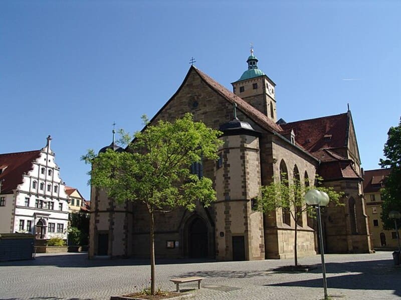 Historische Kirche mit hohem Satteldach und Turm auf einem sonnigen Platz in Schweinfurt.