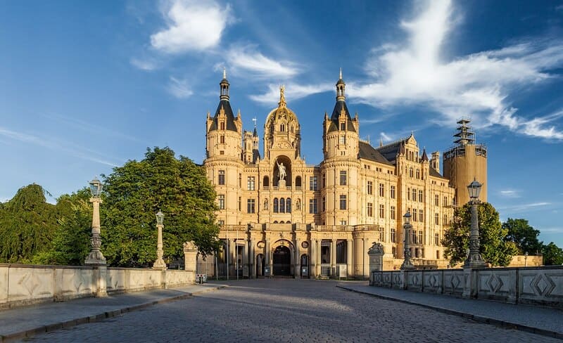 Coreflow-Schwerin-Hero Blick auf das Schweriner Schloss mit Türmen, reich verzierten Fassaden und breiter Steinbrücke im Vordergrund